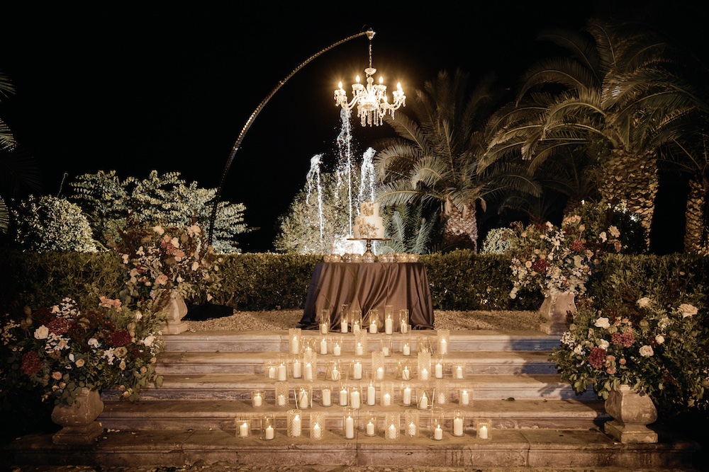 In questa foto il tavolo della torta nuziale decorato con candele e portacandele in vetro disposti su una scalinata in marmo