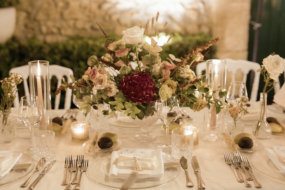 In questa foto il dettaglio di una tavola mariage allestita con coppe di vetro con fiori bordeaux e segnaposto   con nastri di chiffon di colore grigio