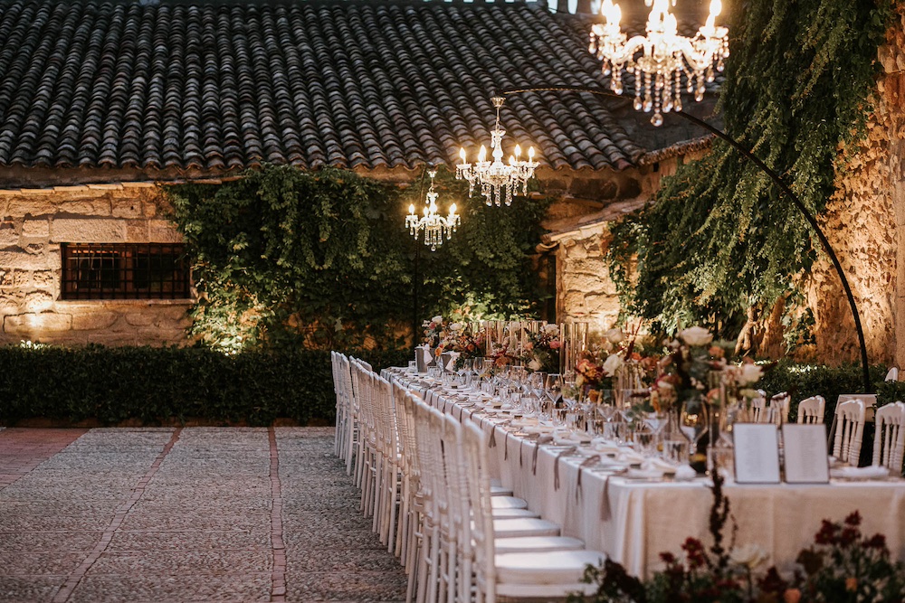 In questa foto un tavolo imperiale allestito con coppe di fiori di colore bordeaux e rose Playa e rose cappuccino e sormontato da lampadari chandelier