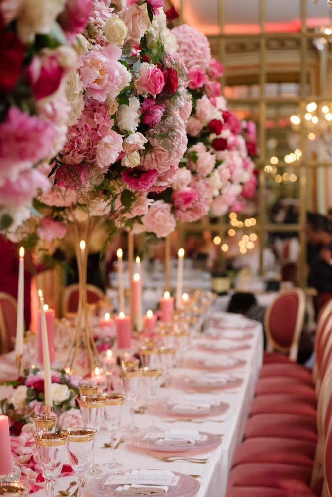 In questa foto un tavolo imperiale decorato dalla Wedding Planner Barbara Vissani con alzate di fiori di colore rosa e fucsia, candele en pendant, piatti trasparenti, bicchieri bordati d'oro, sedie di velluto di colore rosso