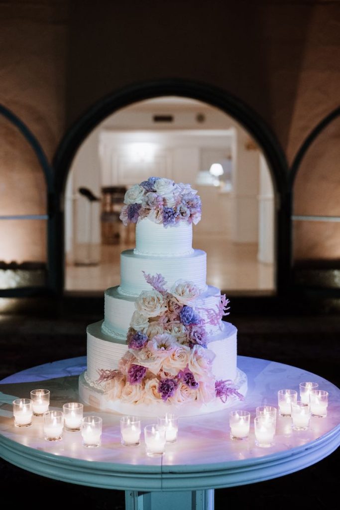 In questa foto una torta nuziale a piani decorata con fiori di colore lilla e bianco e piccole tealight