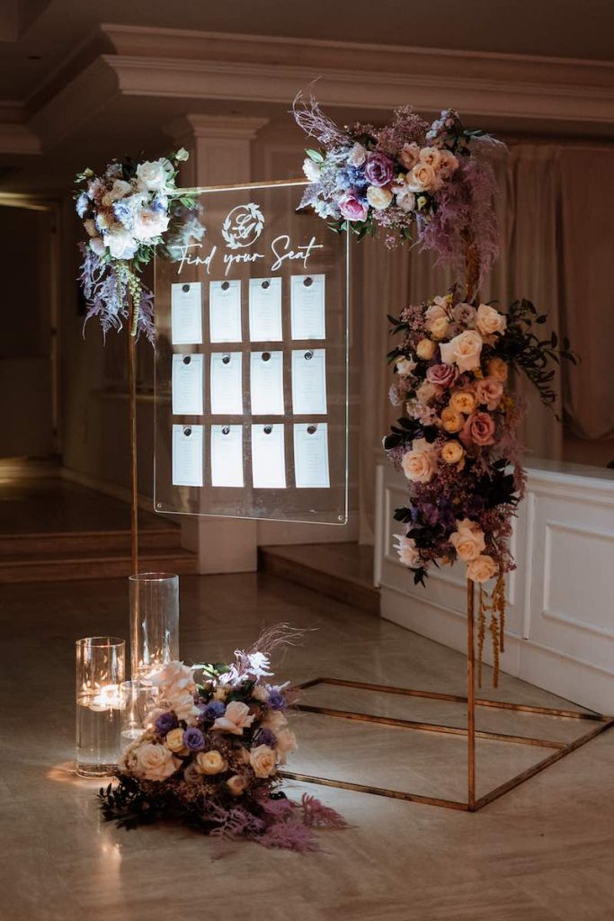 In questa foto un tableau de mariage con pannello in plexiglass decorato con fiori di colore lilla e bianco