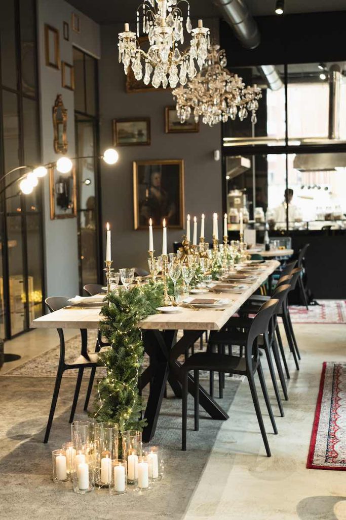 In questa foto un tavolo rettangolare decorato con candele, sedie di colore nero e un runner di pino