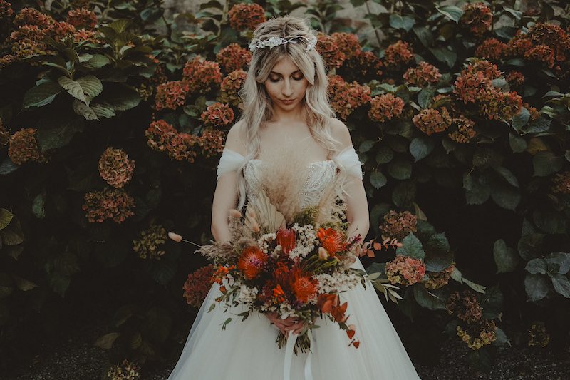 In questa foto di Fabio Betelli una sposa guarda il suo bouquet di fiori rossi circondata da ortensie en pendante