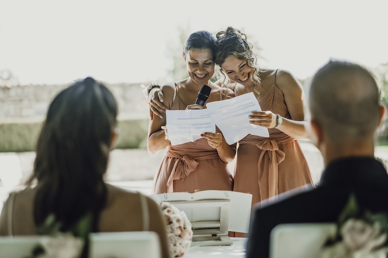 In questa foto di Fabio Betelli due sposi di spalle mentre le damigelle sorridono leggendo i loro discorsi di nozze