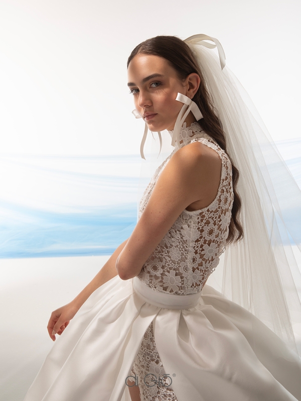 In questa foto la modella indossa un abito da sposa con tuta corta di pizzo floreale e sovragonna firmato le spose di Giò 2024.