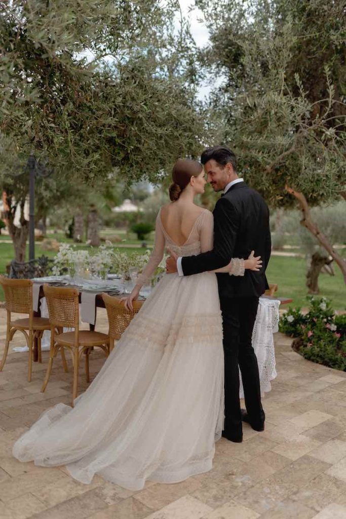 In questa foto due sposi ritratti di spalle si abbracciano e si guardano davanti ad un tavolo allestito per le loro nozze nel giardino di Villa del Gattopardo