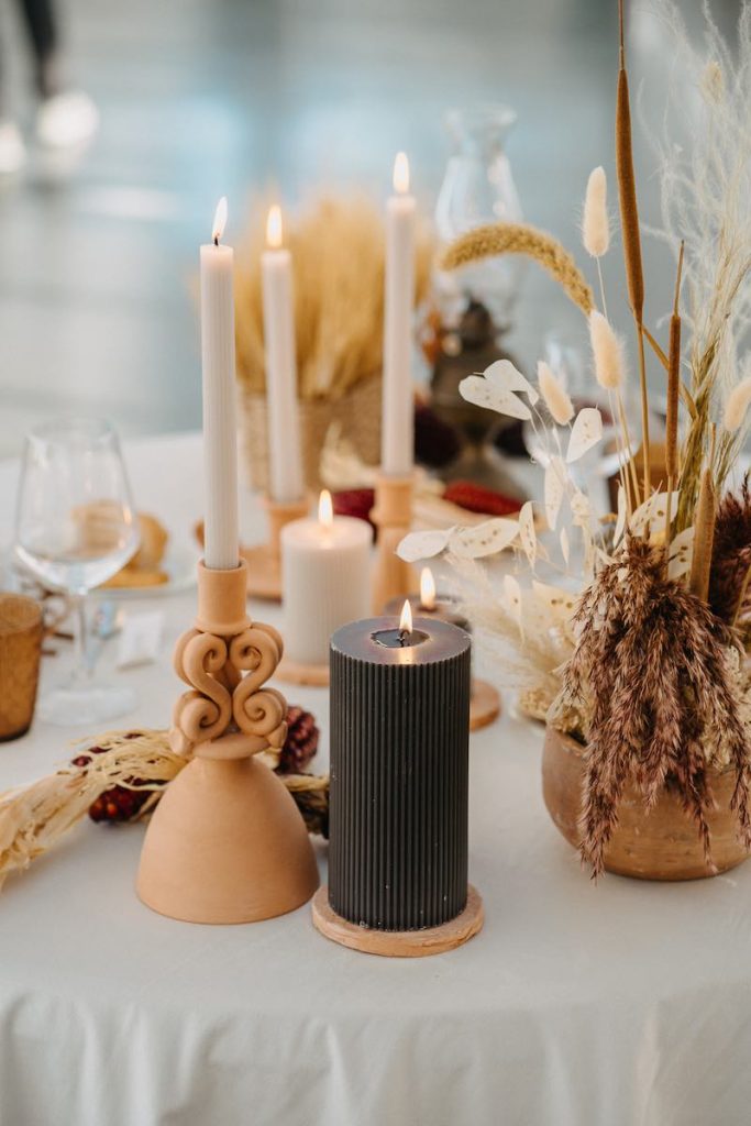 In questa foto un dettaglio di mise en place del matrimonio di Tamara ed Enzo sviluppata da NoidueWedding con candele di colore grigio antracite e bianco, candelabri di terracotta e fiori secchi