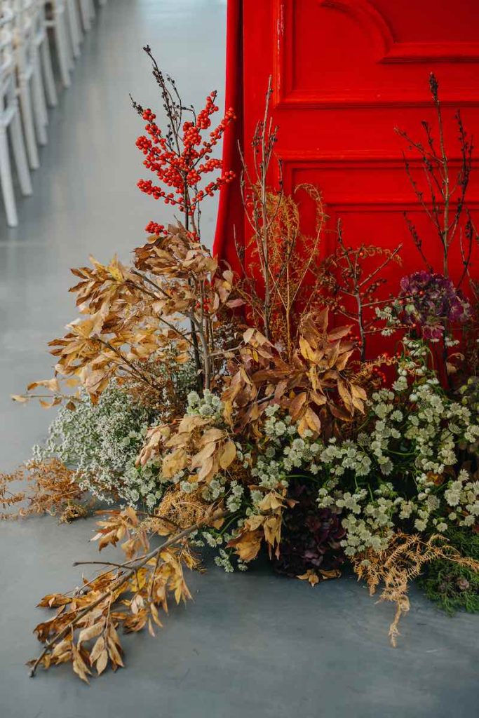 In questa foto il dettaglio di una composizione di foliage e bacche posta davanti ad una porta di colore rosso nella sala del banchetto di nozze di Enzo e Tamara