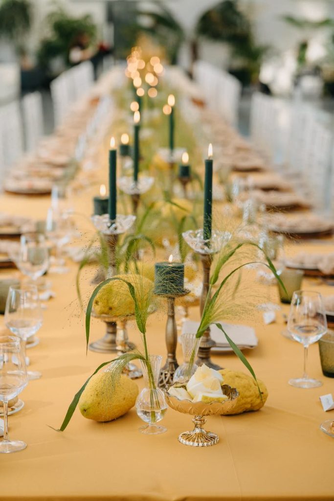 In questa foto un tavolo imperiale per matrimonio allestito da NoidueWedding con tovaglia di colore giallo, candele di colore verde scuro, cedri e portacandele di colore bronzo