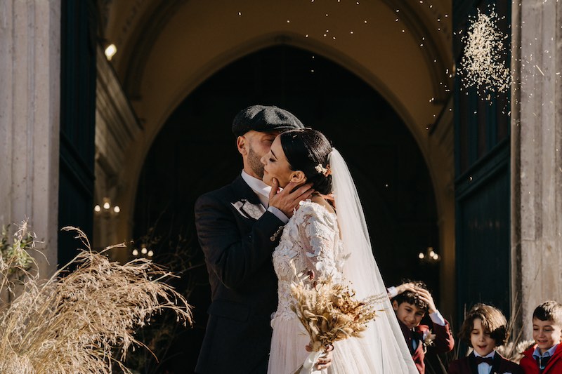 In questa foto due uno sposo abbraccia e bacia una sposa davanti all'ingresso della chiesa dove è stato celebrato il loro matrimonio