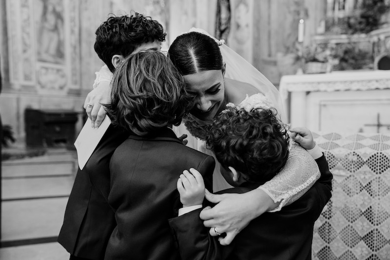 In questa foto in bianco e nero una sposa abbraccia i suoi tre figli
