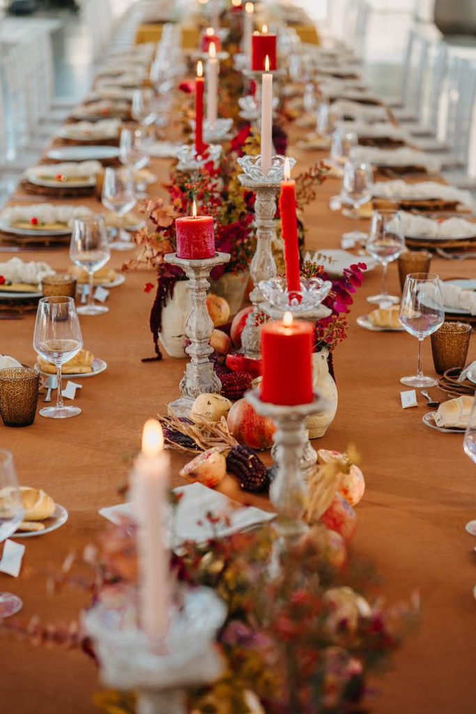 In questa foto un tavolo imperiale di matrimonio allestito da NoidueWedding con candele di colore rosso e bianco panna, portacandele di terracotta, melograni e tovagliato color senape