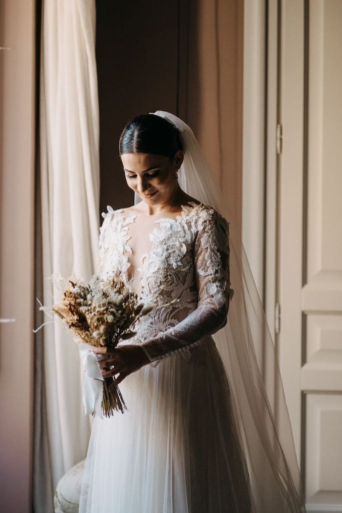 In questa foto una sposa inquadrata mentre guarda il suo bouquet di fiori secchi e stabilizzati di colore beige e panna