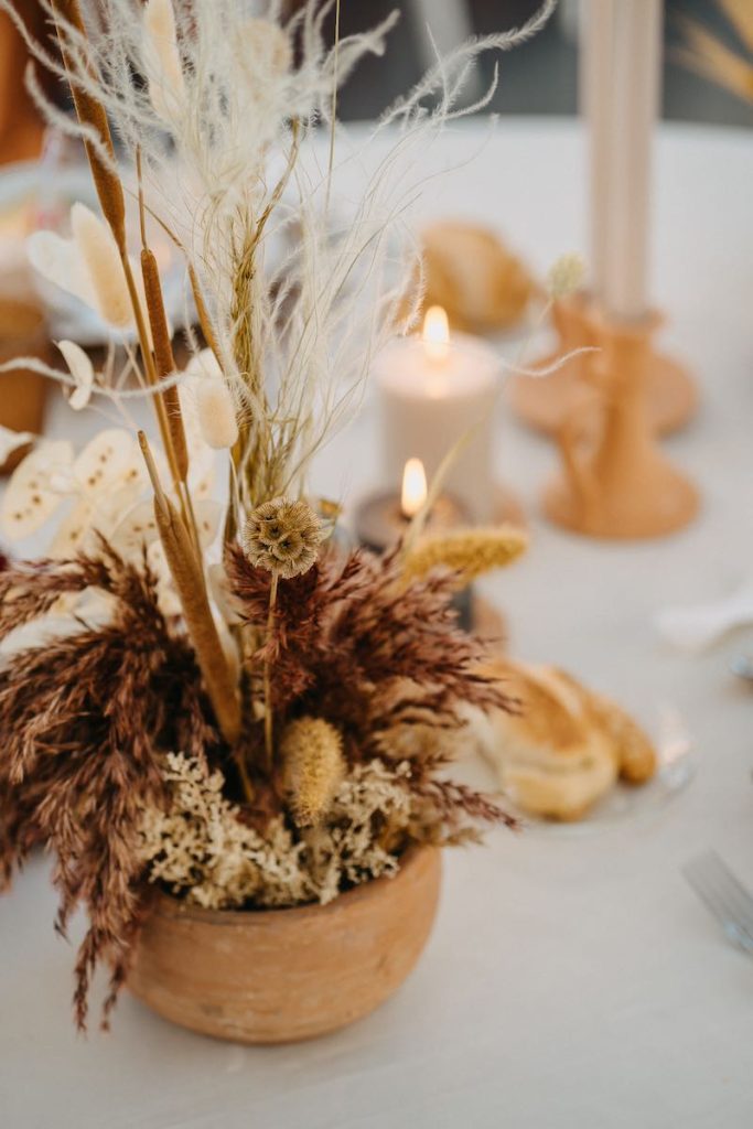 In questa foto un dettaglio di mise en place di nozze realizzata da NoidueWedding con fiori secchi e stabilizzati di colore beige e bainco panna , candele e candelabri di terracotta