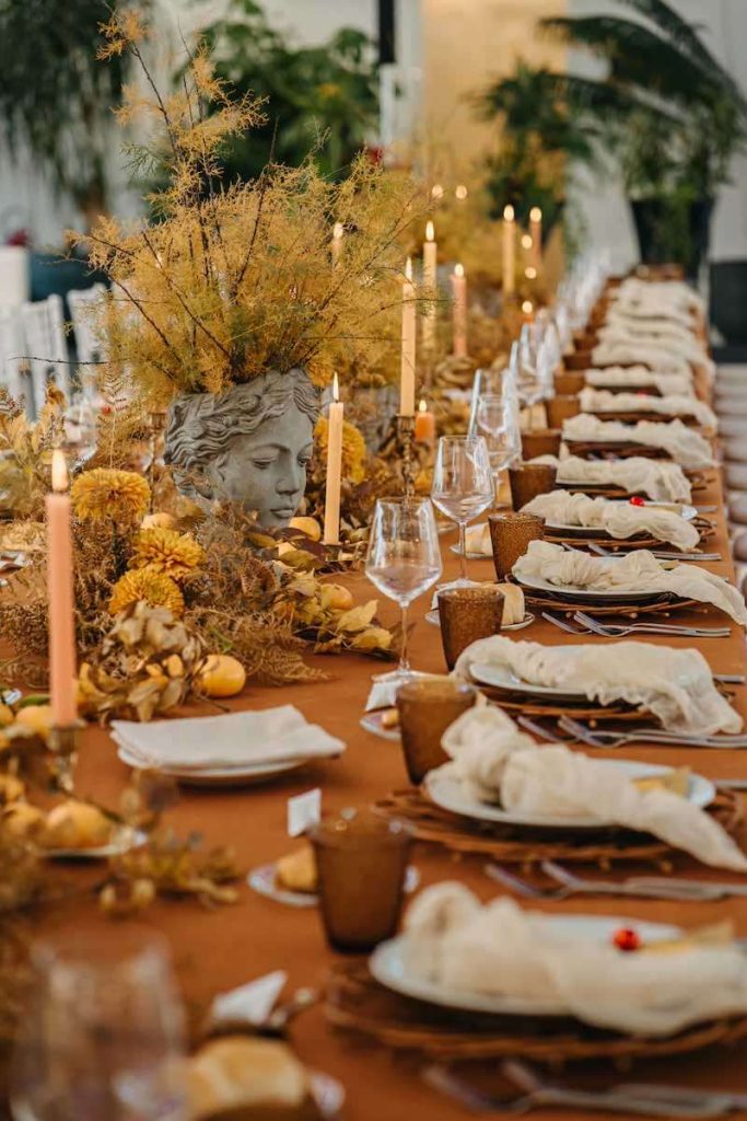 In questa foto un tavolo imperiale di matrimonio allestito da NoidueWedding con candele di colore giallo, portacandele di terracotta, mandarini e tovagliato color ruggine