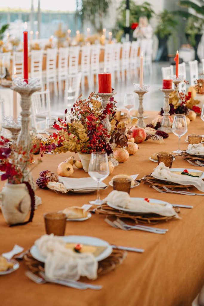 In questa foto un tavolo imperiale di matrimonio allestito da NoidueWedding con candele di colore rosso e bianco panna, portacandele di terracotta, melograni e tovagliato color senape