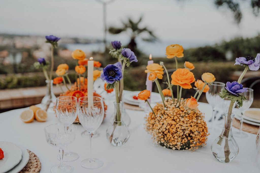 In questa immagine centrotavola floreali, per nozze romantiche, realizzati con vasetti pieni di pochissimi fiori.