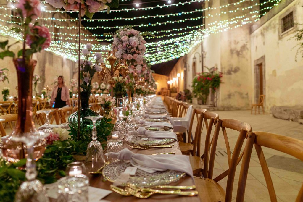 In questa immagine una mise en place matrimonio 2024 con tocchi dorati e fiori che si sviluppano in altezza. 