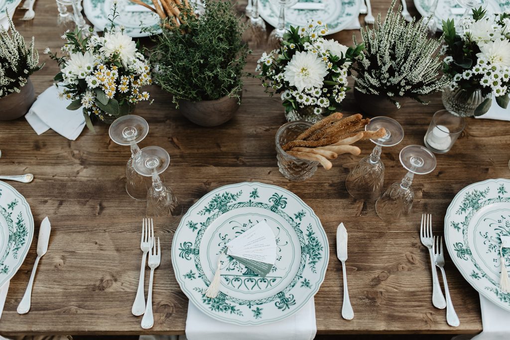 In questa immagine una mise en place matrimonio 2024 con plance nude in legno e piatti nelle tonalità del bianco e del verde. 