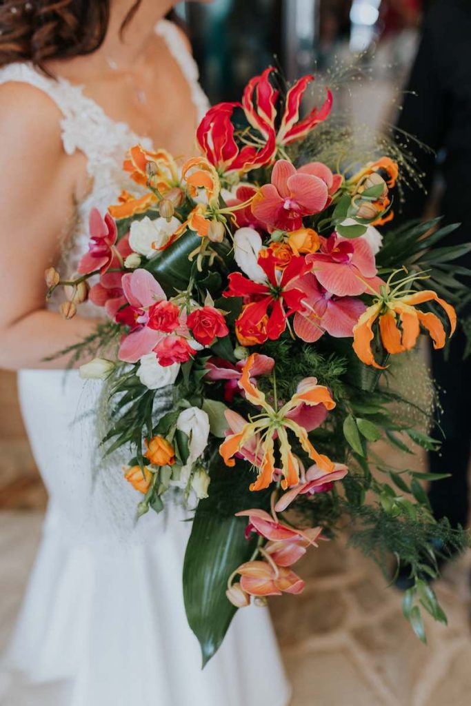 In questa foto un bouquet da sposa a cascata con fiori di gloriosa di colore arancione e fucsia, orchidee fucsia, lisianthus di colore bianco e rose spray fucsia e orange