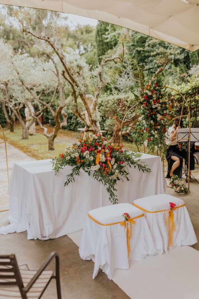 In questa foto l'allestimento del tavolo della cerimonia di nozze di Francesco e Simona composto da una grande decorazione floreale di colore arancione, giallo, fucsia e verde un backdrop abbinato