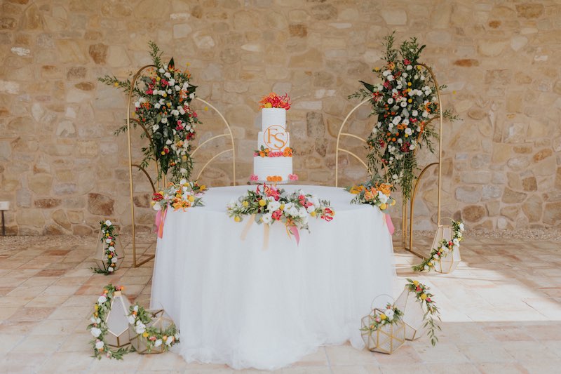 In questa foto il tavolo della torta nuziale degli sposi Francesco e Simona. La scenografia è composta da un backdrop di pannelli 3D di colore oro decorati con fiori di colore bianco, arancione. fucsia e giallo