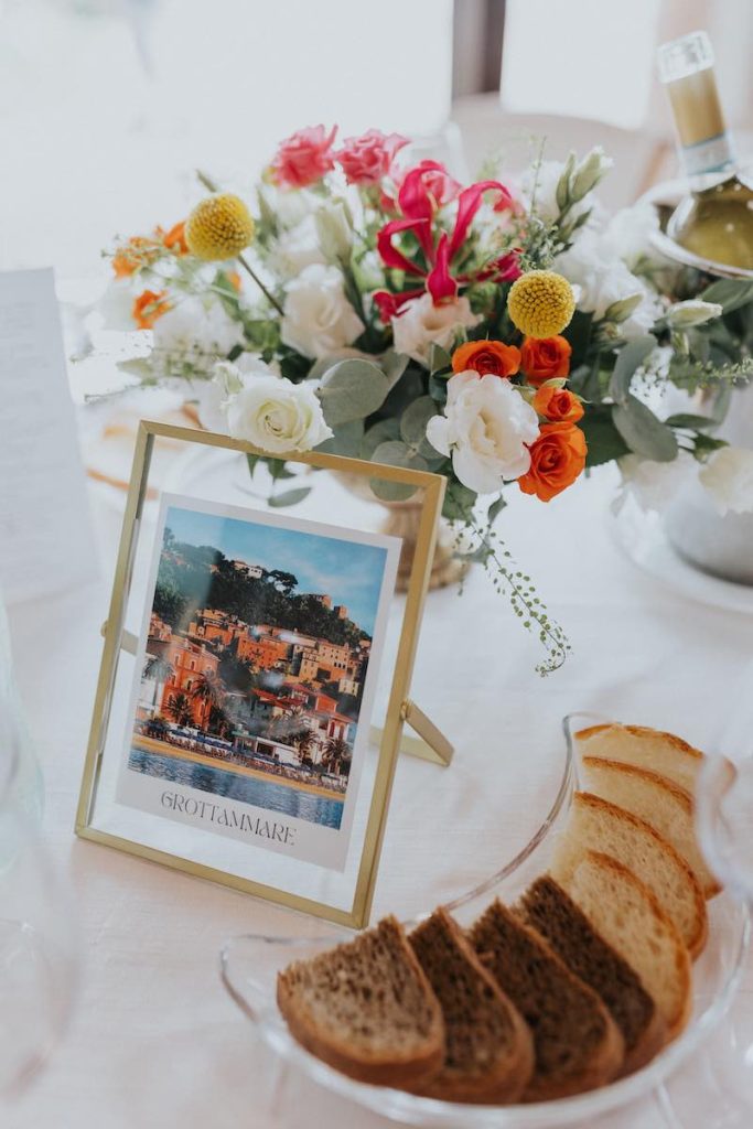 In questa foto uno dei segnatavolo delle nozze di Francesco e Simona composto da cornici dorate nelle quali Elisabetta Alexis ha inserito le immagini dei luoghi più belli delle Marche e dell’Abruzzo e una coppa dorata con fiori di colore arancione, bianco, giallo e fucsia