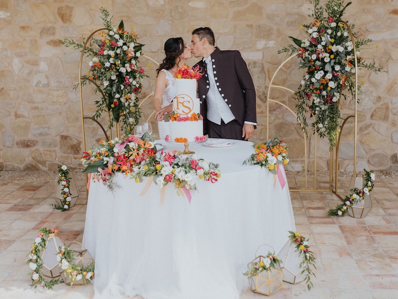 In questa foto gli sposi Francesco e Simona si danno un bacio dietro al tavolo della torta nuziale la cui scenografia è stata progettata da The Bride by Elisabetta Alexis