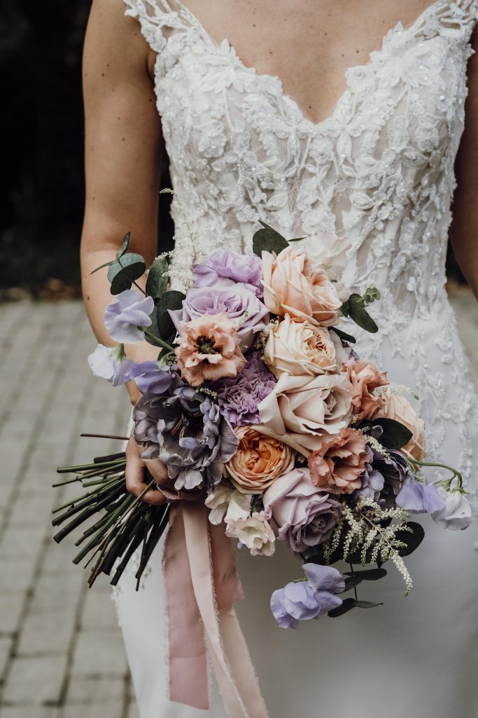 In questa immagine un bouquet sposa 2024 con rose aperte nelle tonalità del lilla, pesca e rosa. 