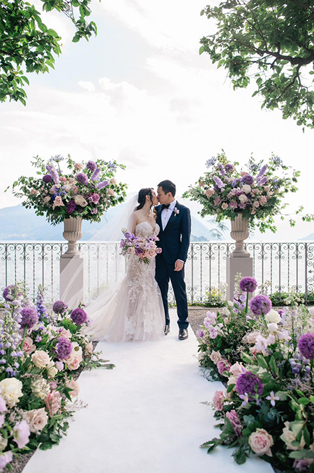 In questa foto due sposi si baciano circondati da fiori viola e lilla