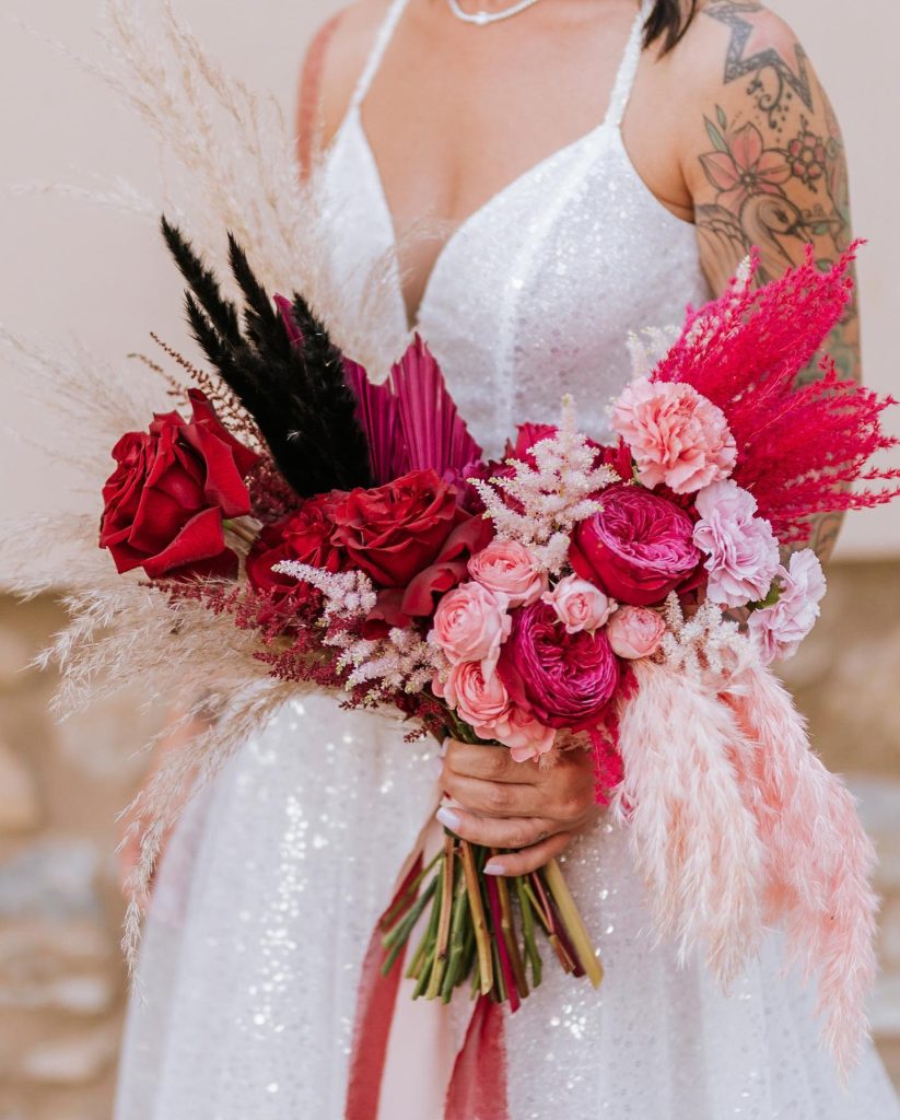 In questa foto una sposa con un bouquet di fiori fuxia e rossi