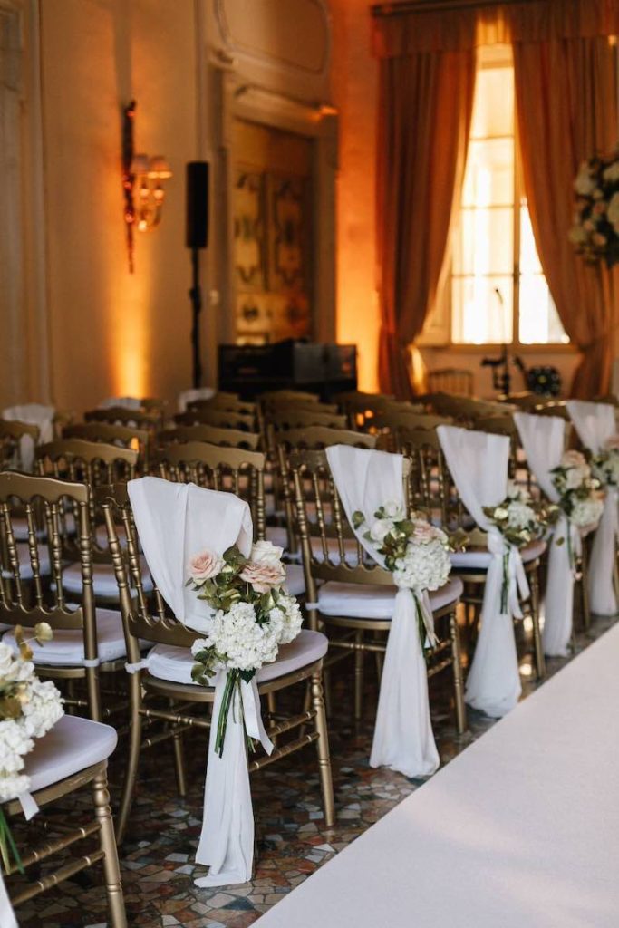 In questa foto il dettaglio dell'allestimento di un matrimonio civile in una sala decorata con rose cappuccino e ortensie di colore bianco legate a un drappo di stoffa di colore bianco a sedie dorate