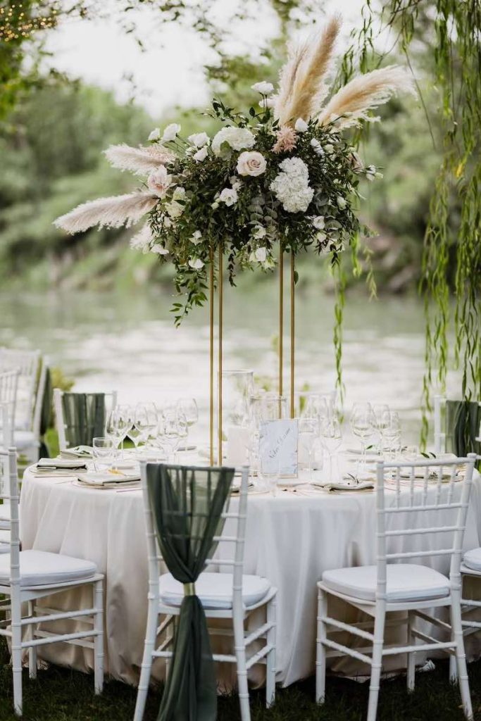 In questa foto un tavolo per matrimonio allestito con pampas e fiori di colore bianco. Sulle sedie la Wedding Planner Nives Malvestiti ha disposto tre drappi di lino di colore verde