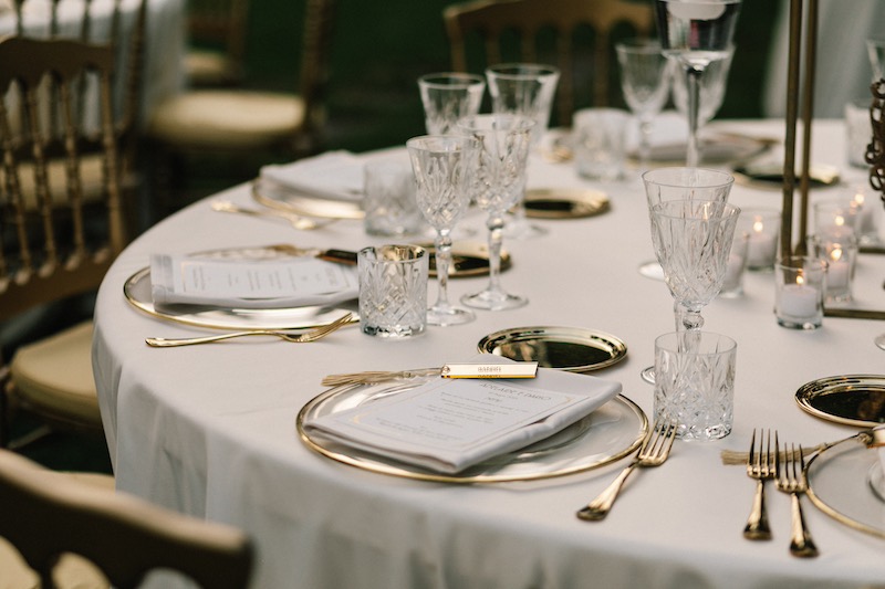 In questa foto il dettaglio di una mise en place elegante con posate dorate e piatti in porcellana con bordo oro e segnaposto en pendant