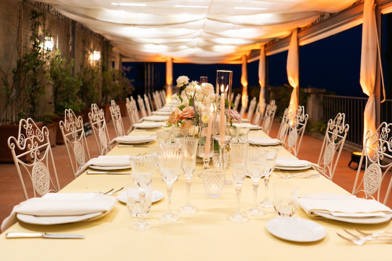 In questa foto un tavolo imperiale da matrimonio allestito da Benedetta Carpanzano con tovagliato colore giallo paglierino, tovaglioli colore rosa cipria, candele di colore rosa, fiori en pendant e sedie in ferro battuto di colore biand