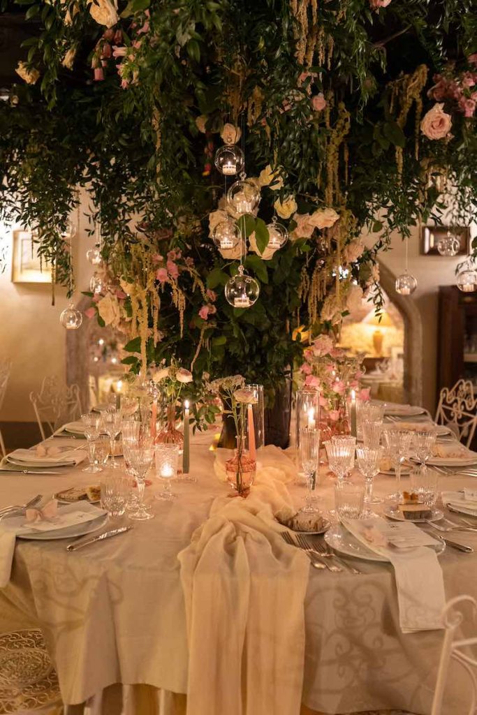In questa foto un tavolo degli sposi sviluppato attorno ad un albero decorato con fiori e candele sospese