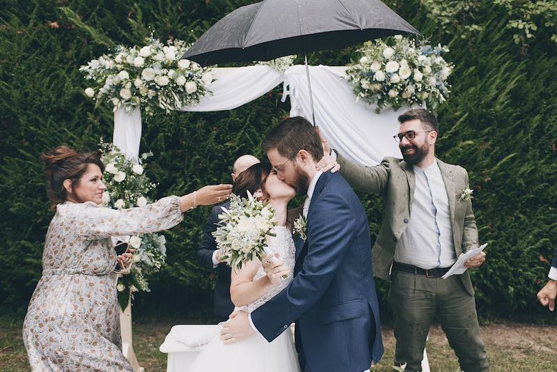 In questa foto di Serena Libutti due sposi si baciano alla fine del rito civile mentre gli amici li coprono con gli ombrelli