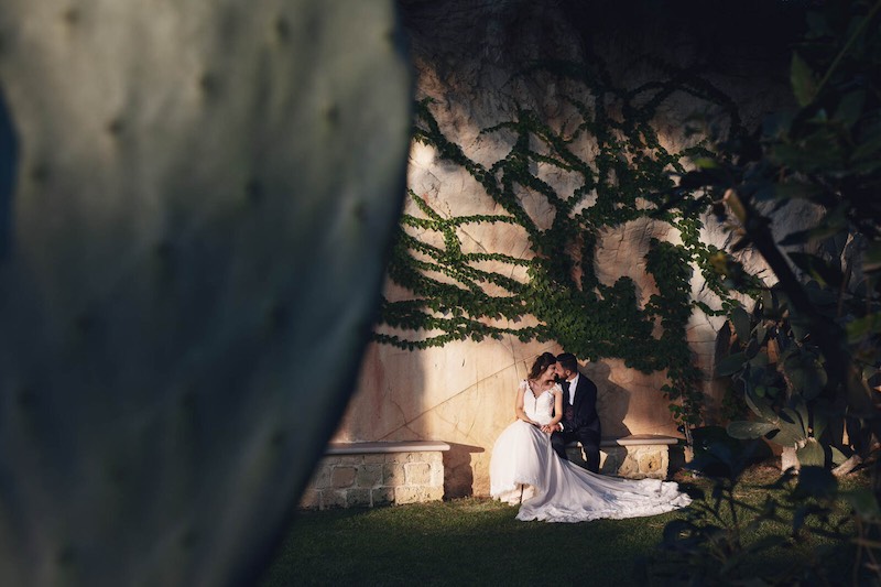 In questa foto due sposi si guardano sorridenti seduti su un muretto in un grande giardino