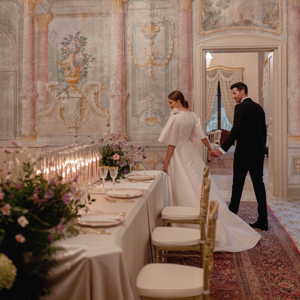 In quesa foto una coppia mentre cammina intorno alla tavola imperiale allestita per il matrimonio, in una delle sale di Villa del Gattopardo, luxury Wedding location a Palermo