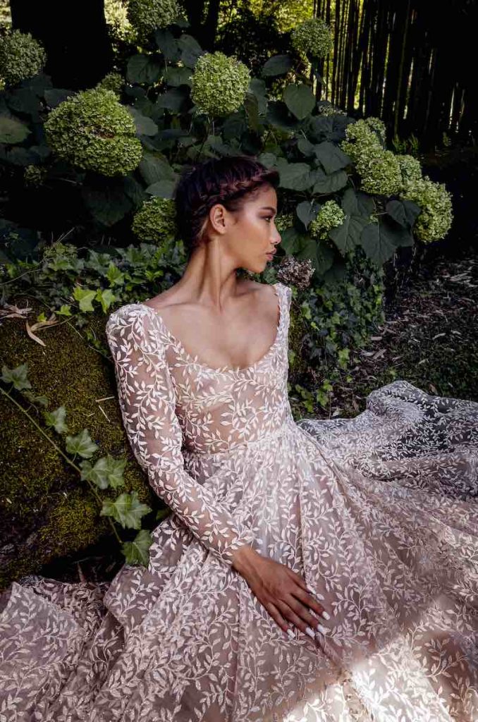 In questa foto una modella con un abito da sposa in pizzo e un'acconciatura sposa con una treccia morbida frontale