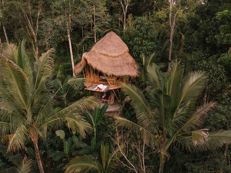 In questa foto una coppia è sdraiata su una piattaforma di un bungalow immerso in una foresta a Bali