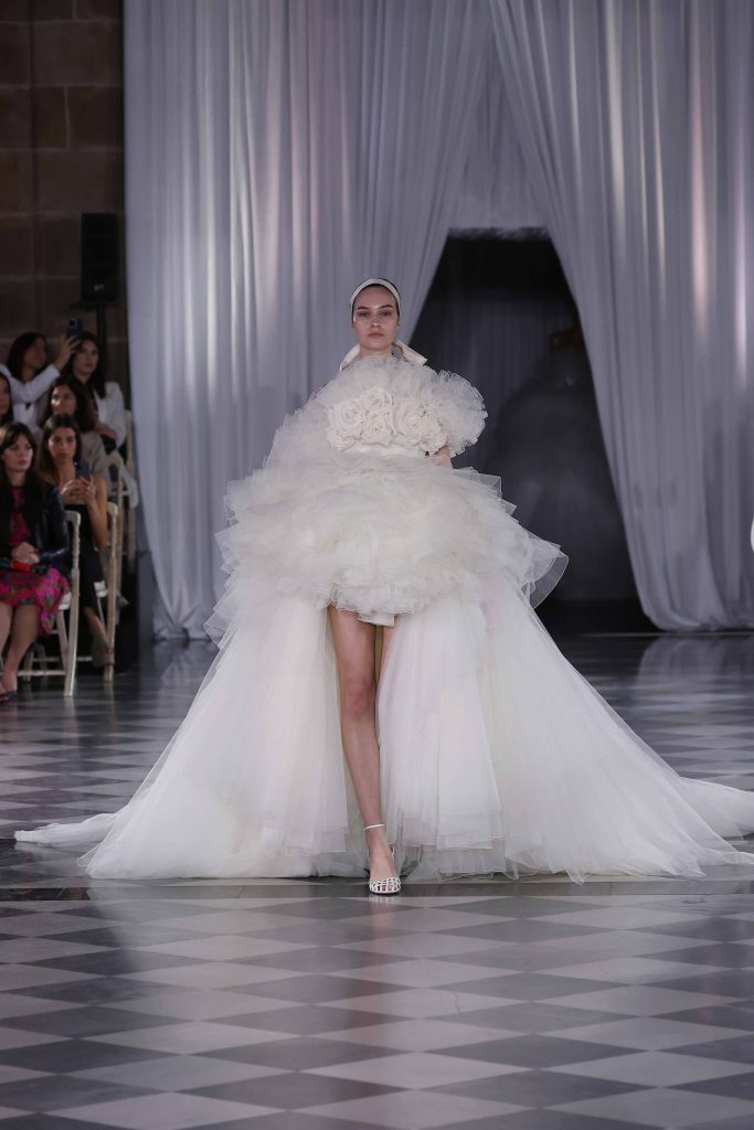 In questa immagine un abito da sposa Giambattista Valli 2025 con gonna corta in tulle e lungo strascico. 