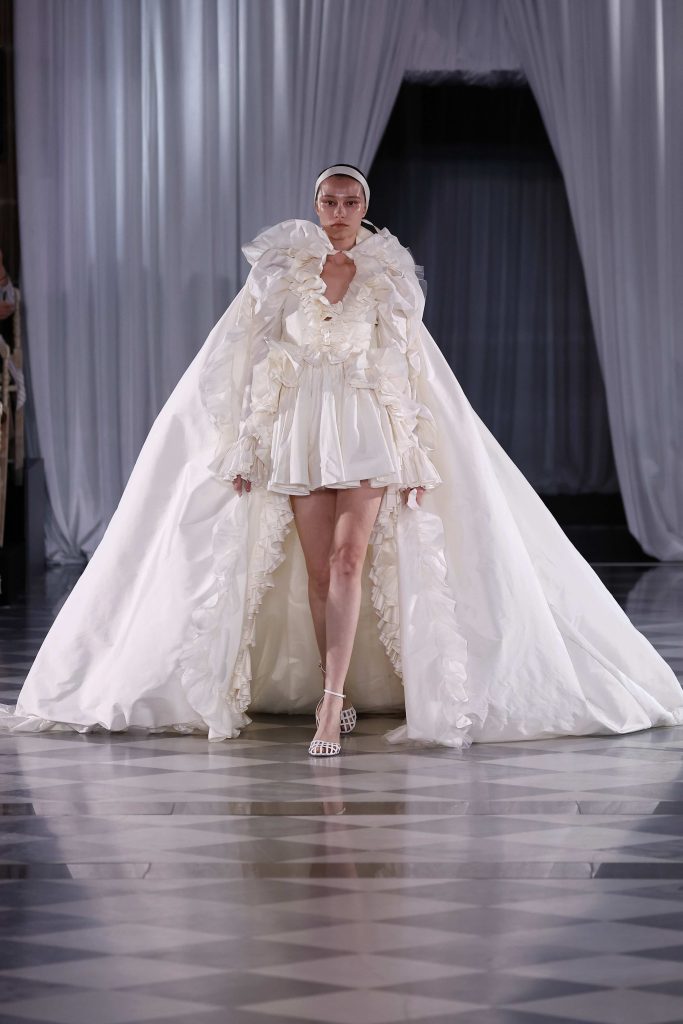 In questa immagine un abito da sposa Giambattista Valli 2025 gonna corta e maxi cappa. 