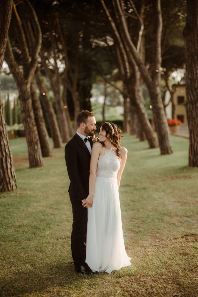 In questa foto di Alessio Bazzichi due sposi si guardano posando in un viale alberato. La sposa si spalle si gira per guardare il suo sposo