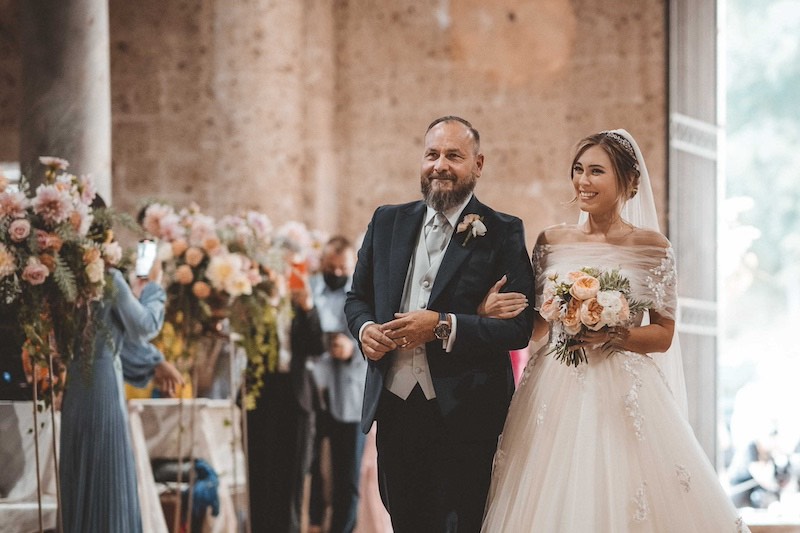 In questa foto di Emiliano Allegrezza una sposa sorride durante il suo ingresso in chiesa al braccio del papà