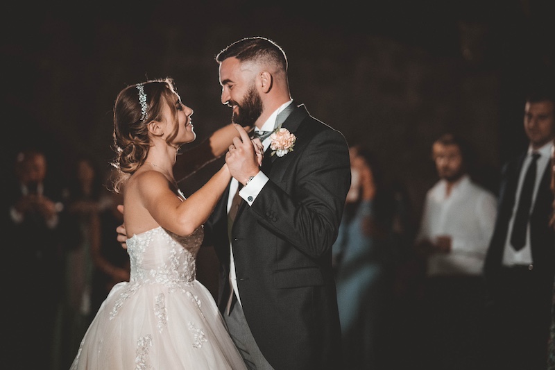 In questa foto di Emiliano Allegrezza, due sposi si guardano negli occhi e sorridono durante il loro primo ballo circondati dai loro ospiti