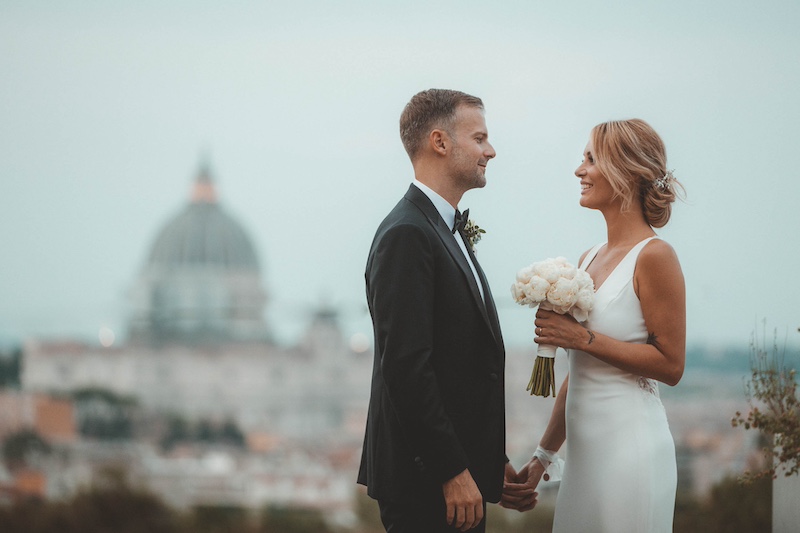 In questa foto di Emiliano Allegrezza due sposi si guardano tenendosi per una mano sullo sfondo di San Pietro