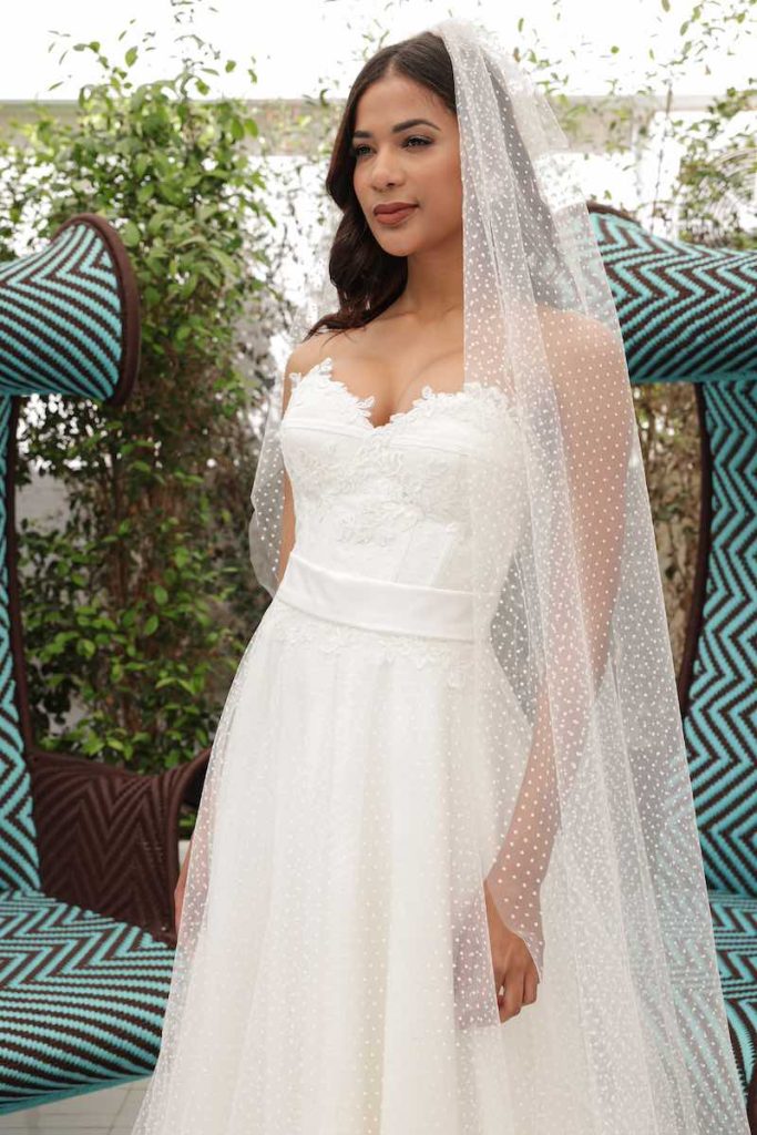 In questa foto una modella indossa un abito da sposa in tulle plumetis con bustier e scollo a cuore e velo abbinato della collezione Mariù di Atelier Benedetta