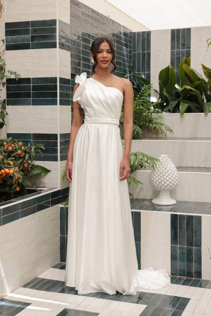 In questa foto una modella indossa un abito da sposa scivolato con scollatura monospalla della collezione Mariù di Atelier Benedetta